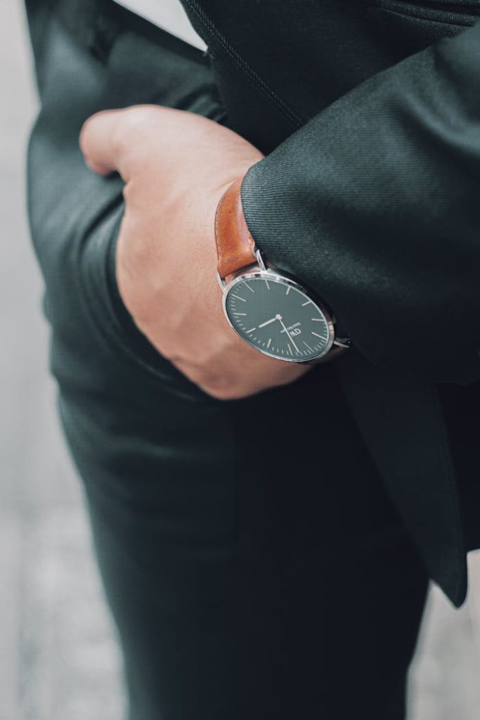 Elegant black dial wristwatch with brown leather strap on man's hand in suit pocket.